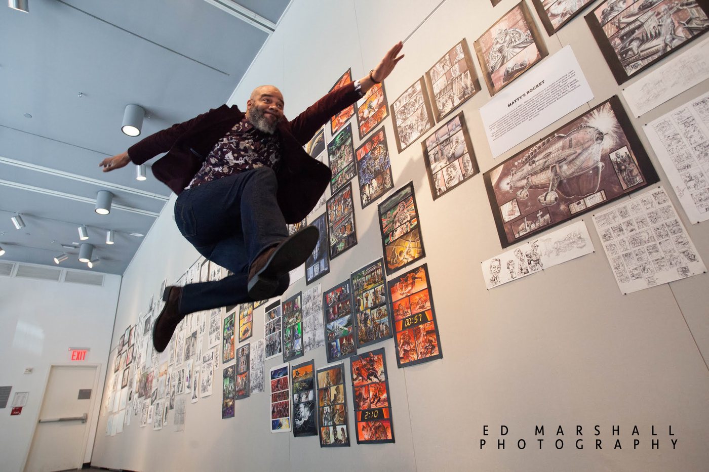 Tim Fielder leaping in front of a gallery wall covered with his Matty's Rocket artwork and storyboards